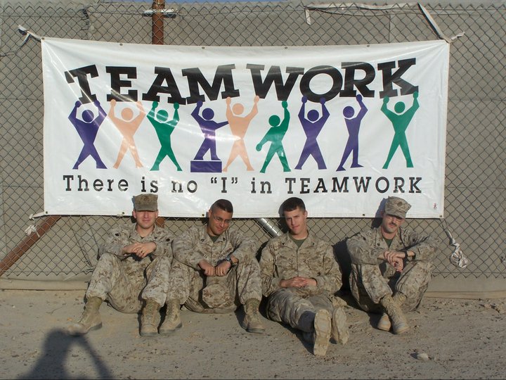 Four Marines sitting below a banner in Fallujah, Iraq